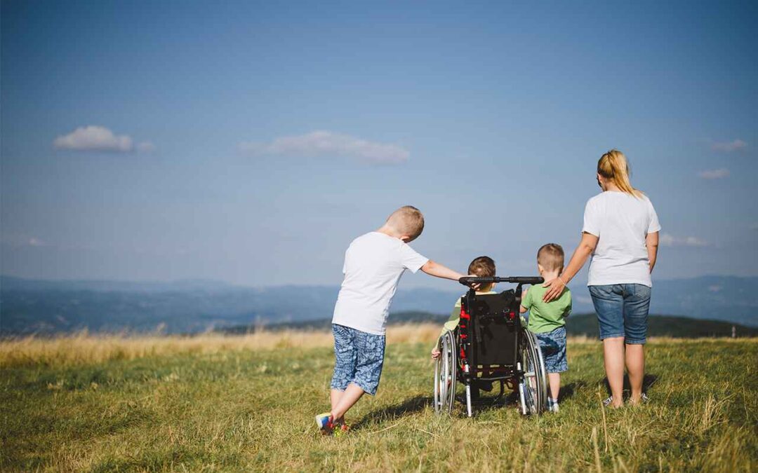 Two children and an adult walking with a child in a wheelchair across a grassy field towards the mountains during an ADA camping trip.