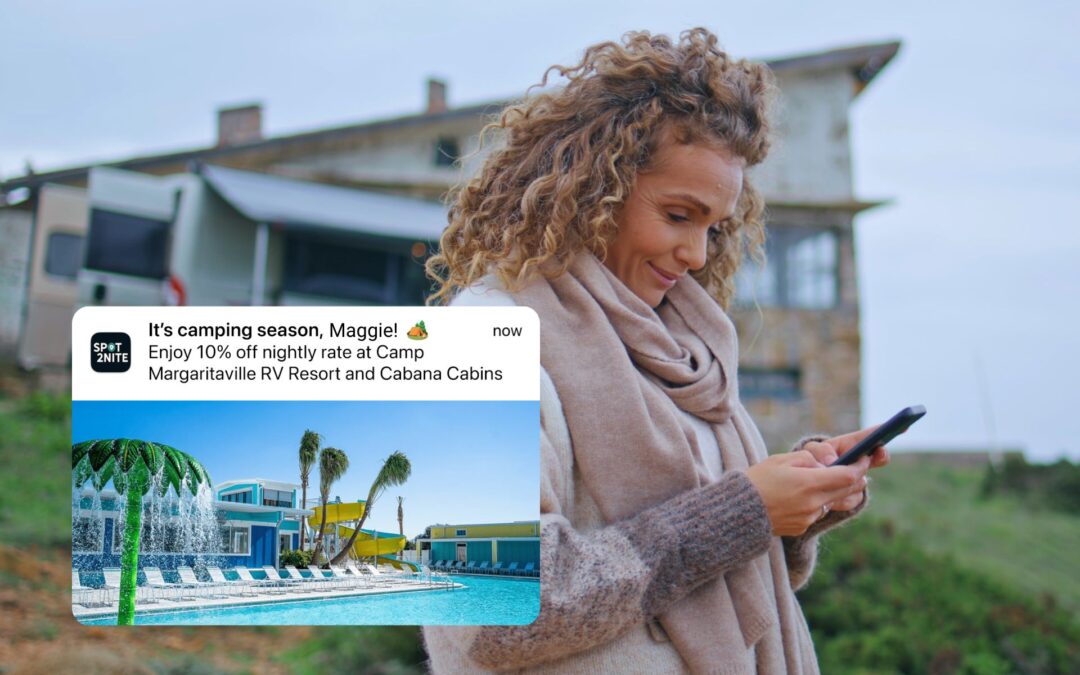 A woman smiles at her phone while reading a mobile push notification from Spot2Nite, with an RV visible in the background.